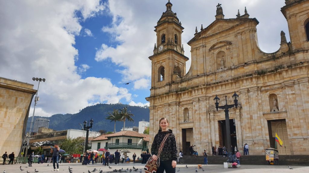 Naomi standing in front of the cathedral on Plaza Simon Bolivar in Bogota. There are mountains in the background.