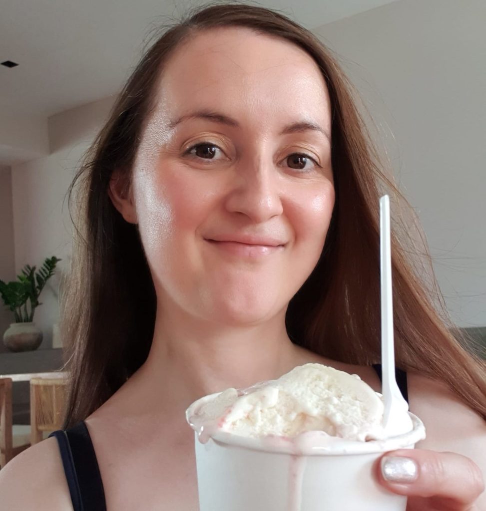 Naomi smiling with her hair down, holding a cheesecake flavored ice cream in a tub in her hand.